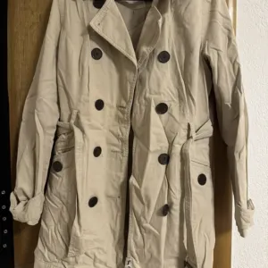 Bež ženski trenč kaput sa duplim kopčanjem