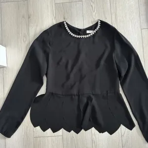 Elegantna crna bluza sa detaljem ogrlice i peplum krojem